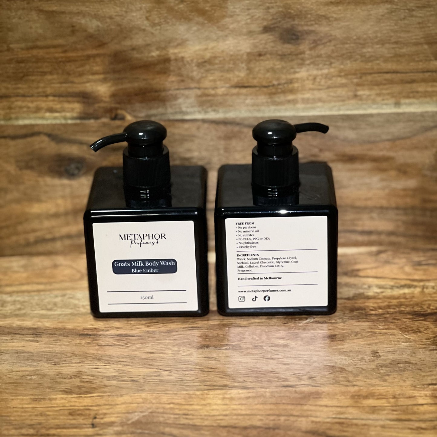 Product image of Metaphor Perfumes goats milk body wash in a black pump bottle on a wooden surface — Blue Ember, inspired by Dior Sauvage.