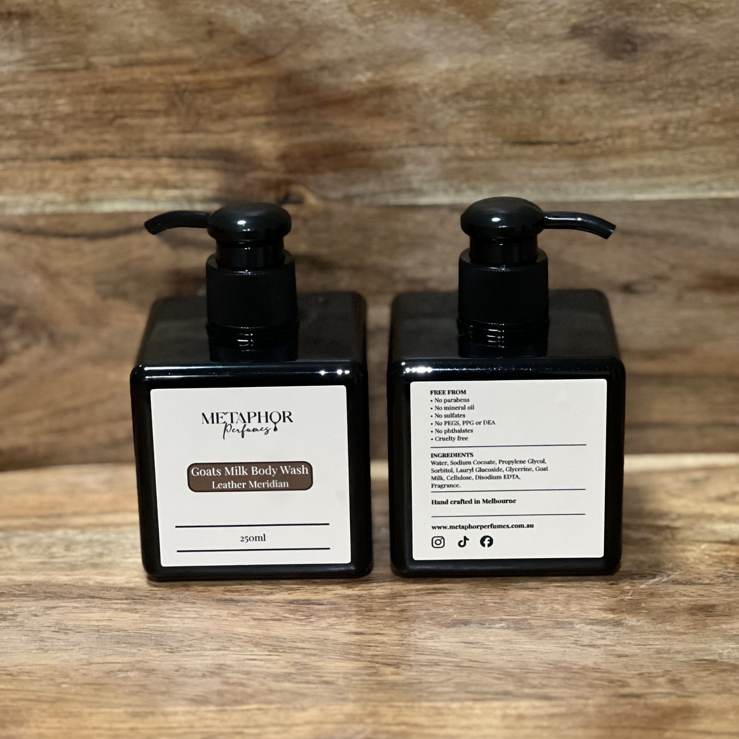 Product image of Metaphor Perfumes goats milk body wash in a black pump bottle on a wooden surface — Leather Meridian, inspired by Tom Ford Ombre Leather.