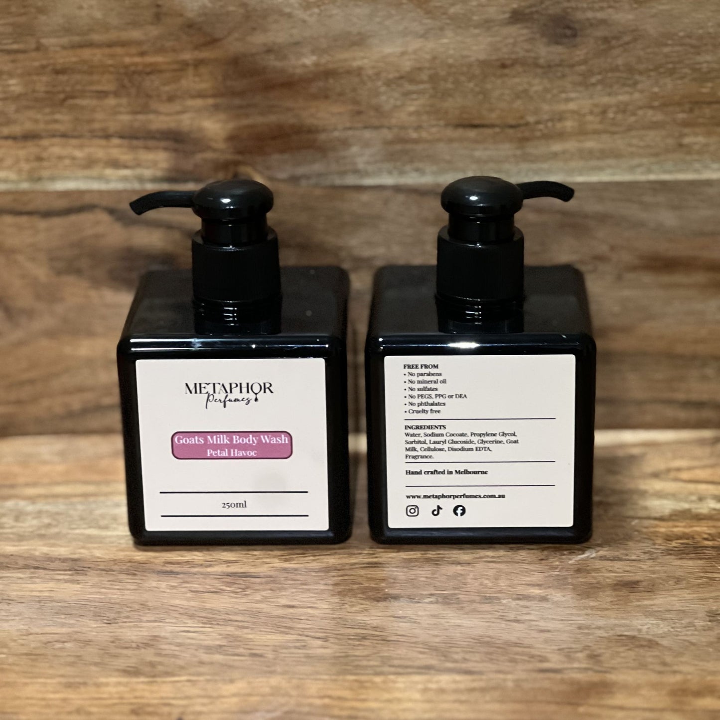 Product image of Metaphor Perfumes goats milk body wash in a black pump bottle on a wooden surface — Petal Havoc, inspired by Viktor & Rolf Flowerbomb.
