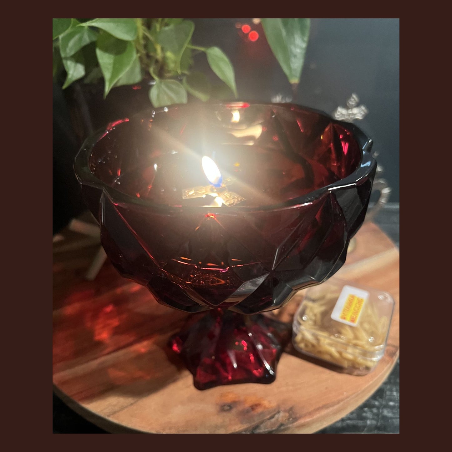 A ruby red chalice used as an olive‑oil wick holder, with a beeswax wick floating and already lit.