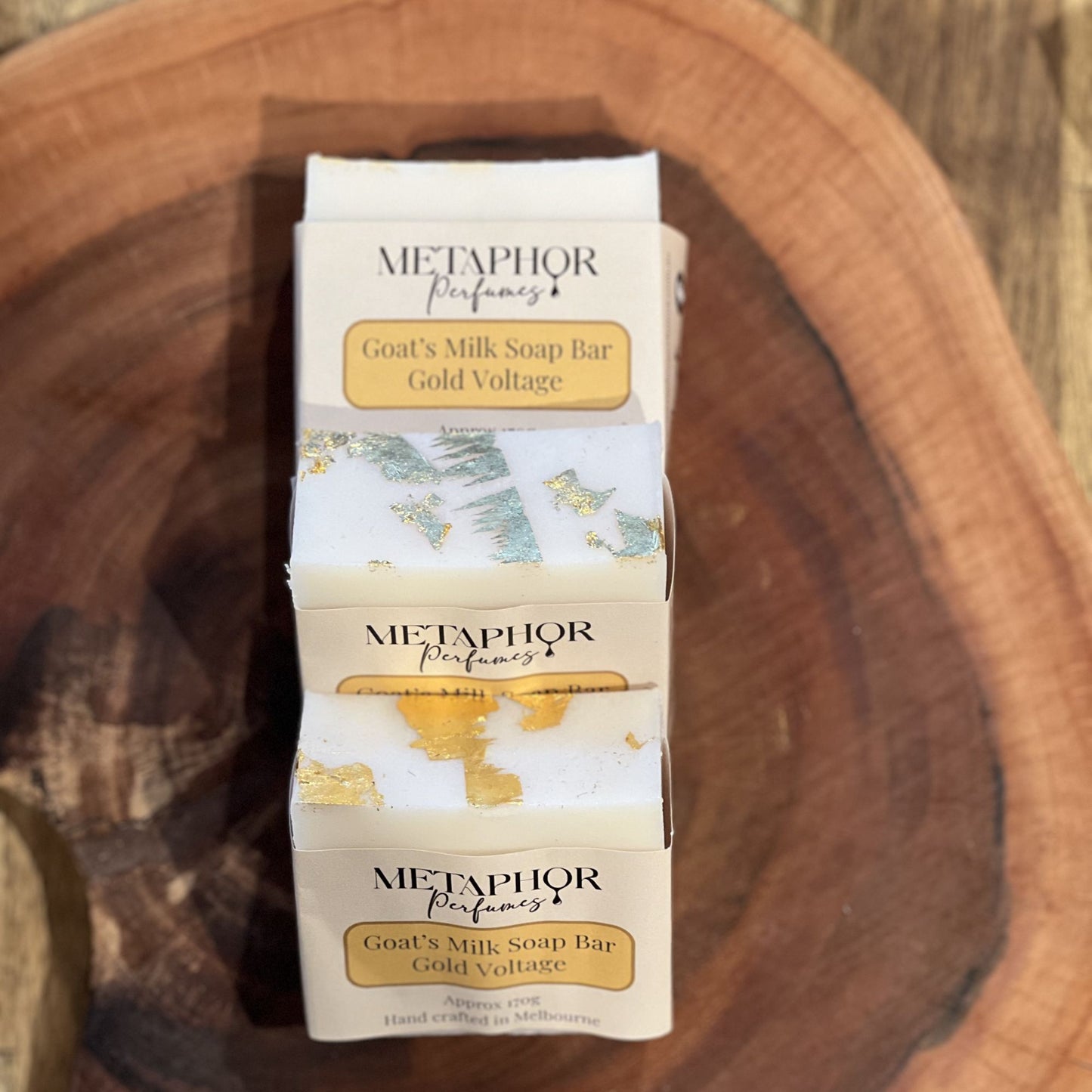 Gold‑topped goat’s milk soap bars wrapped in Metaphor Perfumes Gold Voltage labels, arranged on a wooden surface; inspired by Paco Rabanne 1 Million