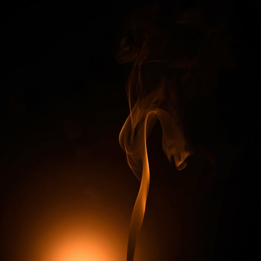 Abstract dark scene with warm golden light and a single plume of illuminated incense smoke rising against a black background, representing the Black Livani candle mood.”
