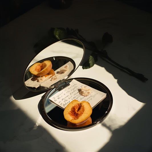 Bloom Edit extrait de parfum — a refined reinterpretation of Creed Spring Flower. Peach, melon, jasmine, rose, musk, and amber. A halved peach reflected in a mirror beside a handwritten note and rose stem, evoking springtime precision and olfactive punctuation.