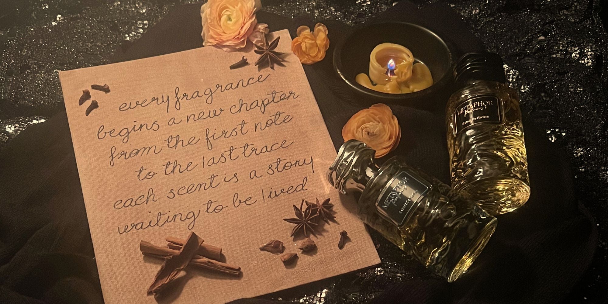 Homepage hero image for Metaphor Perfumes — poetic quote written on aged parchment, surrounded by candlelight, ranunculus, star anise, and perfume bottles resting on soft, shadowed fabric folds.