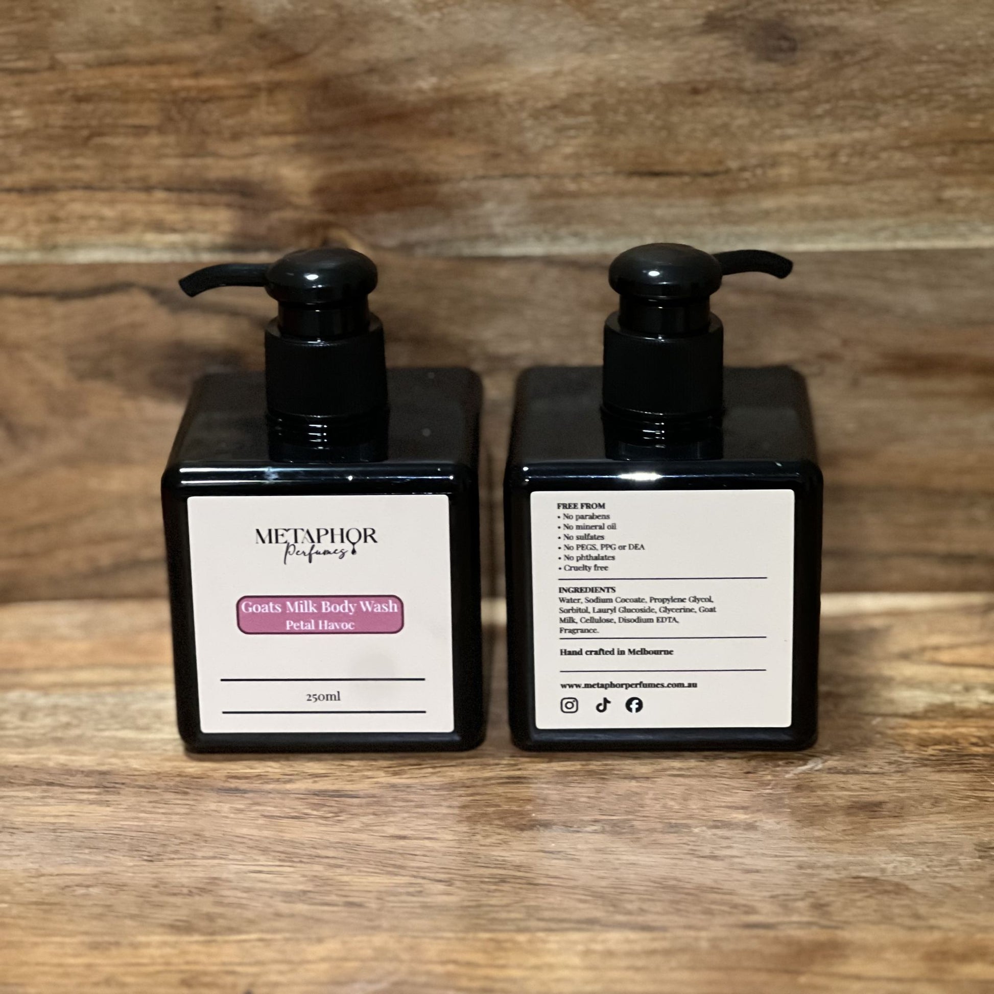 Product image of Metaphor Perfumes goats milk body wash in a black pump bottle on a wooden surface — Petal Havoc, inspired by Viktor & Rolf Flowerbomb.