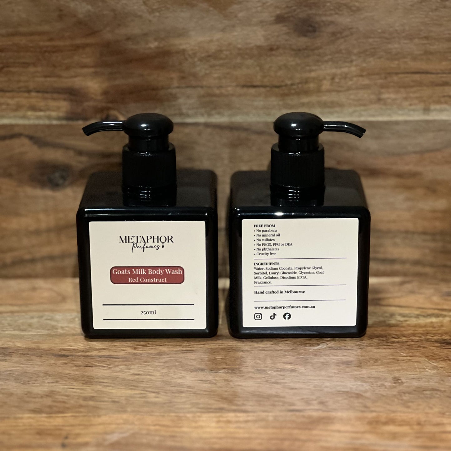 Product image of Metaphor Perfumes goats milk body wash in a black pump bottle on a wooden surface — Red Construct, inspired by MFK Baccarat Rouge 540.