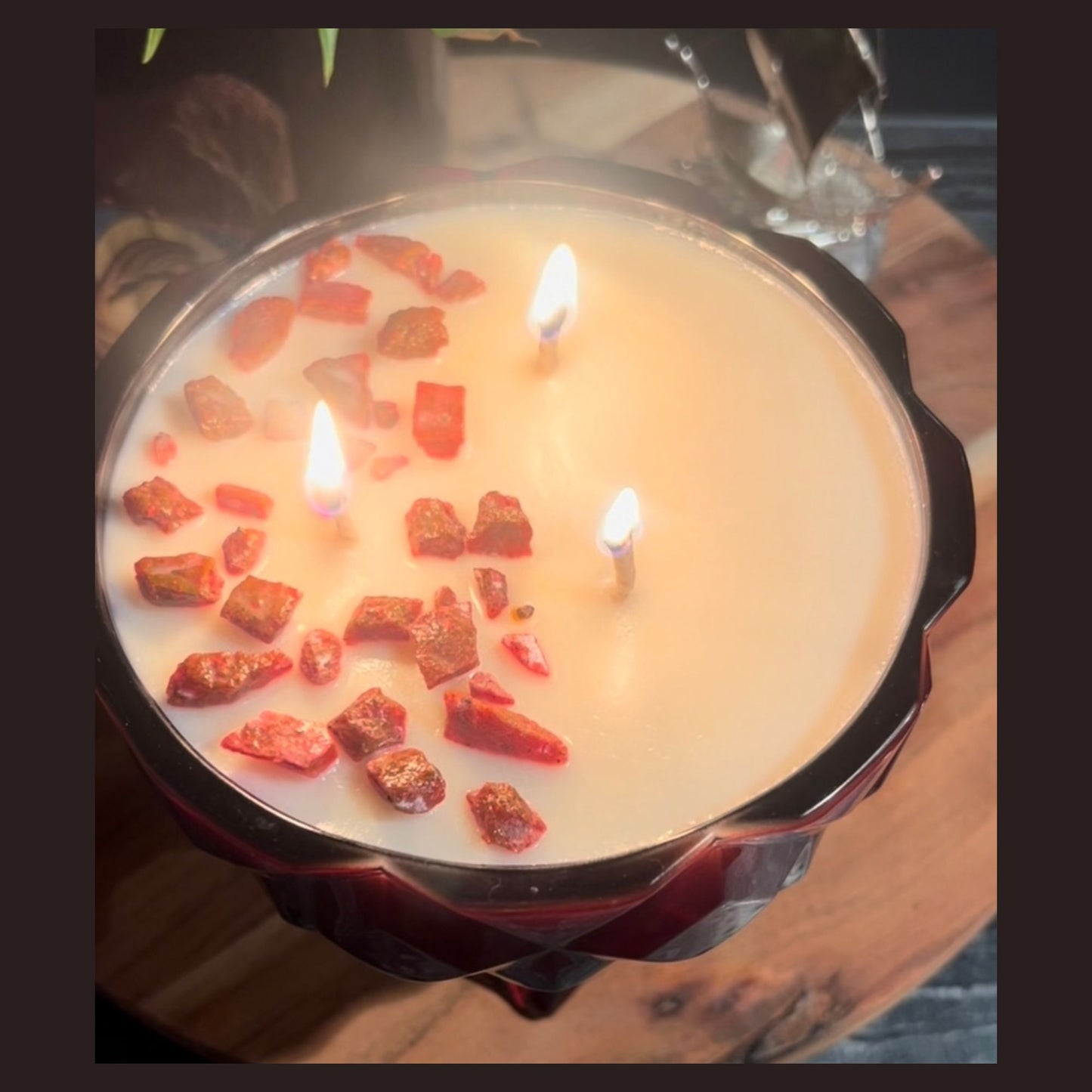 A ruby red chalice candle with white wax and red rose Livani pieces on top, shown unlit on a wooden surface.