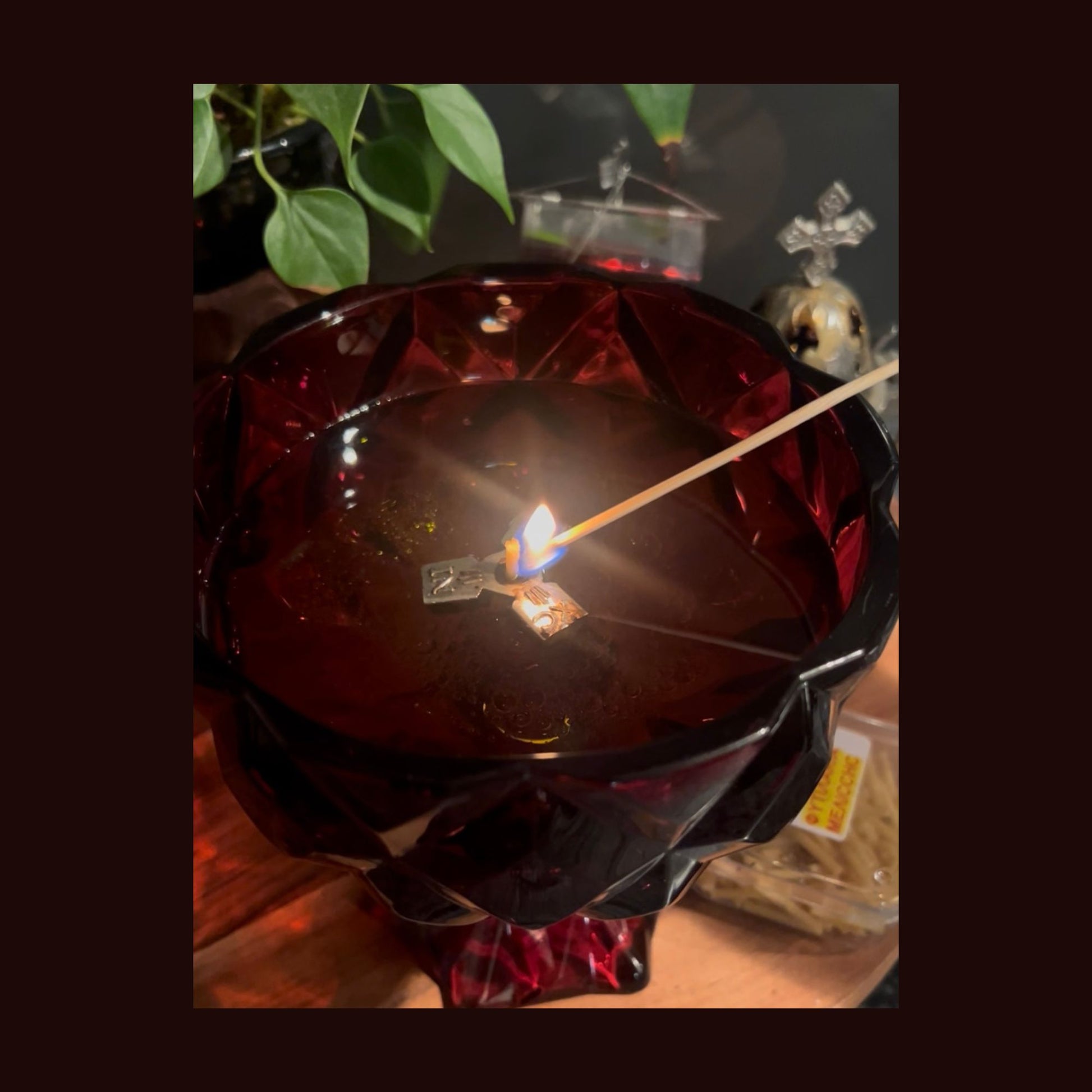 A ruby red chalice candle with melted wax and a floating olive‑oil wick being lit for devotional use.