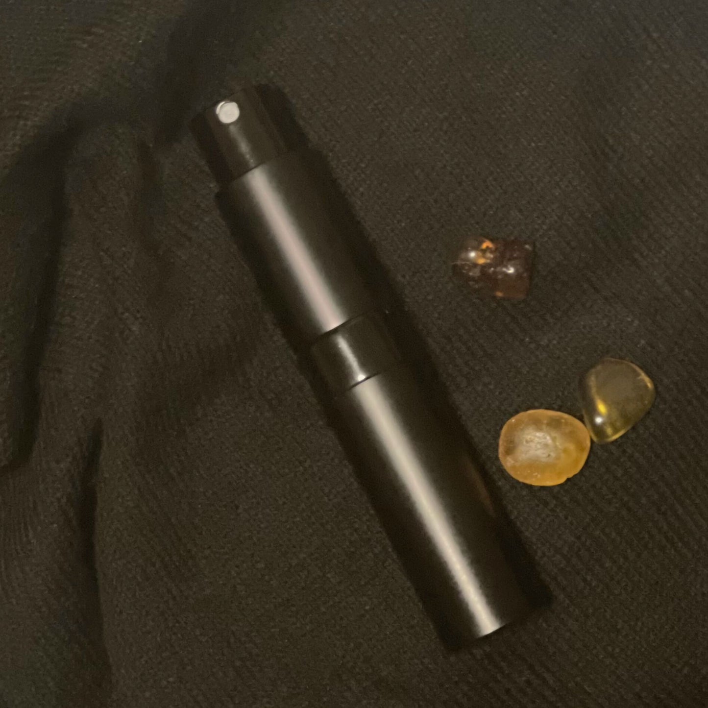 Refillable atomiser for Velvet Zafferano and Saffron Rites, shown with amber pieces on black cotton.