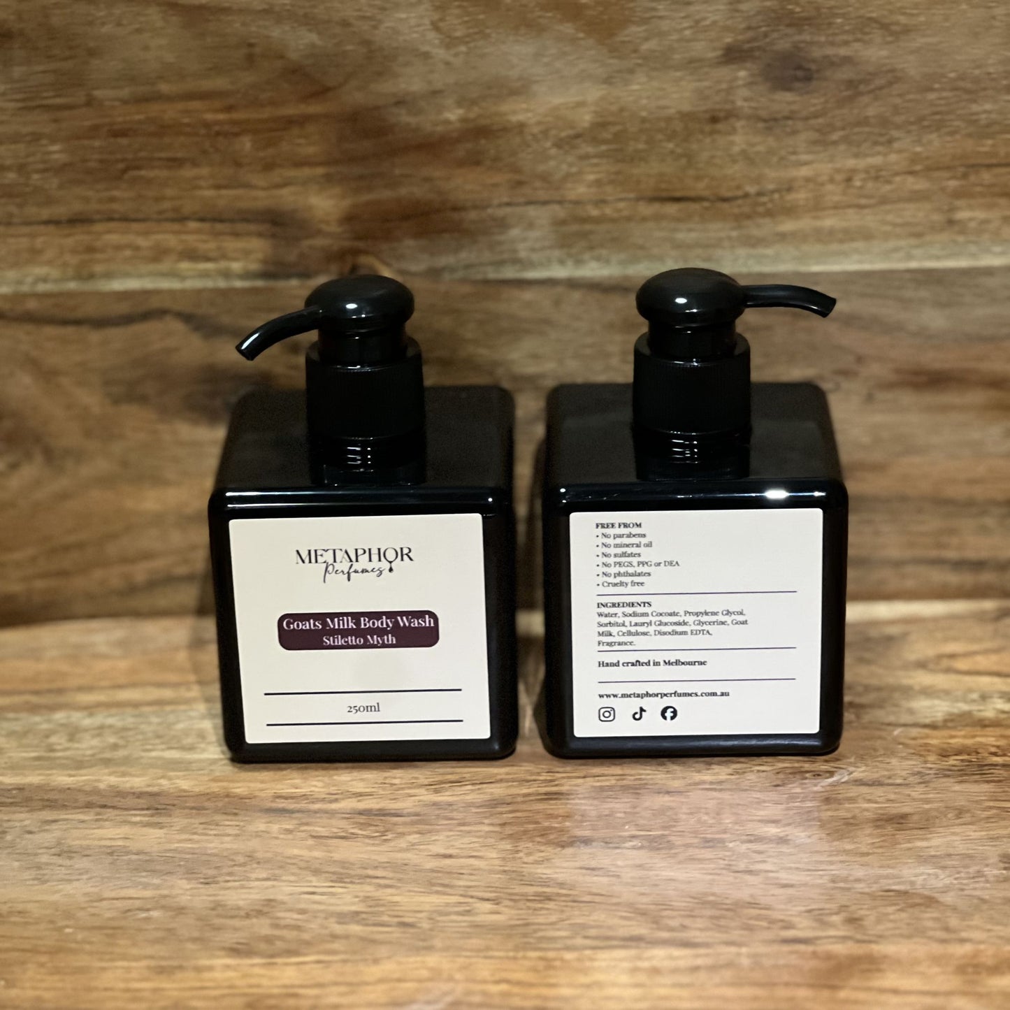 Product image of Metaphor Perfumes goats milk body wash in a black pump bottle on a wooden surface — Stiletto Myth, inspired by Carolina Herrera Good Girl.